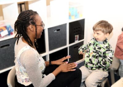 A therapy session with therapists showing child to tap their knees and the child imitating them, smiling