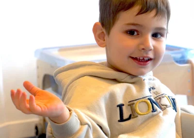 Picture of an autistic little boy smiling and waving at the camera