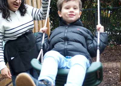 Picture of a happy autistic little boy having fun on a swing, being pushed by his therapist who's having fun and smiling
