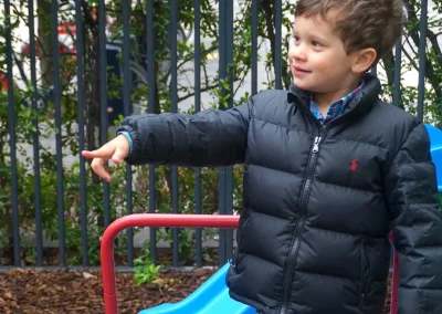 An autistic little boy playing outside and pointing at something while smiling to request and demand - as learned in ABA therapy