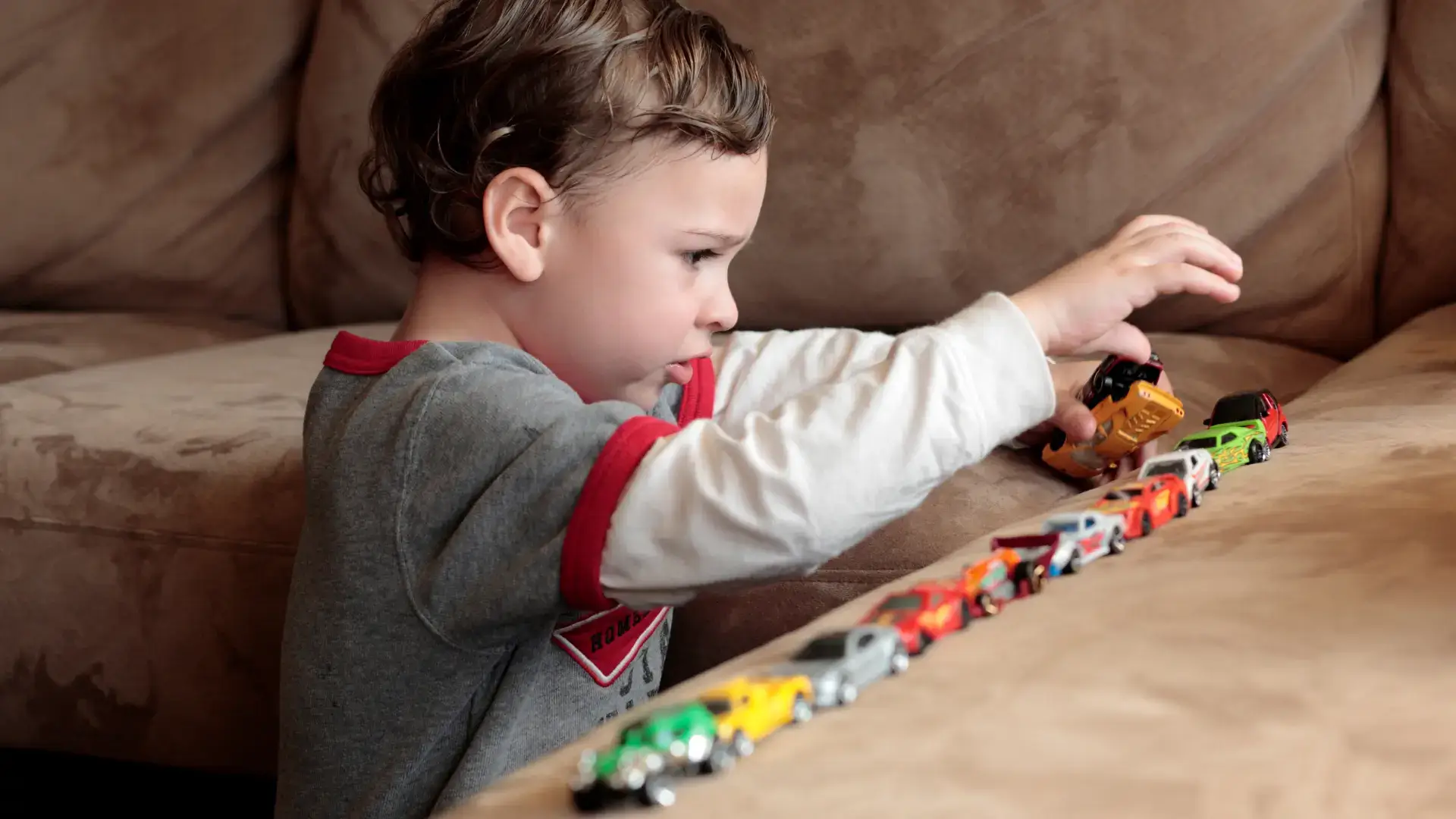 An autistic child playing with car toys and aligning them on the couch