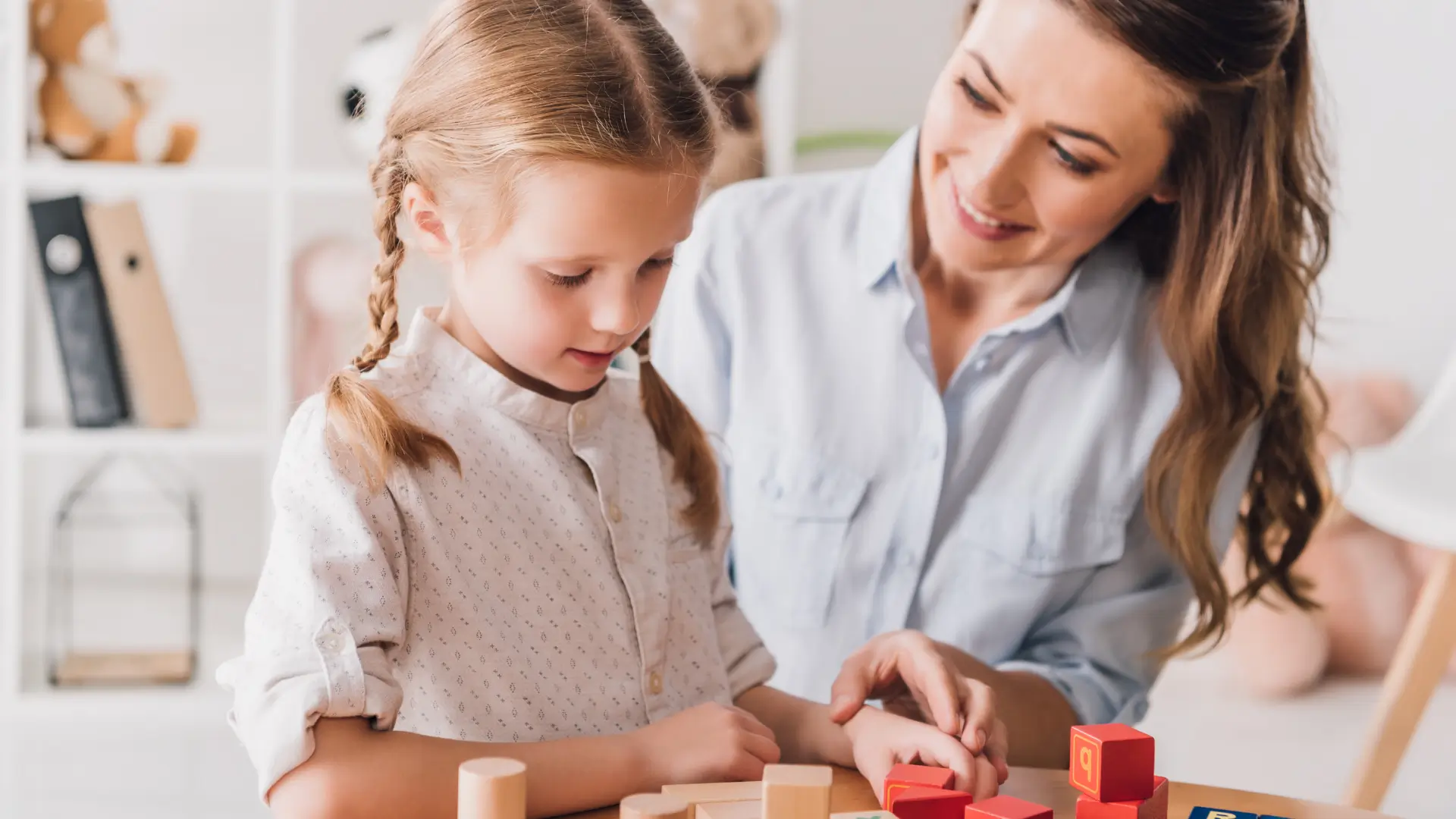 A mom playing with building blocks with her autistic little girl. Both are smiling and looking happy