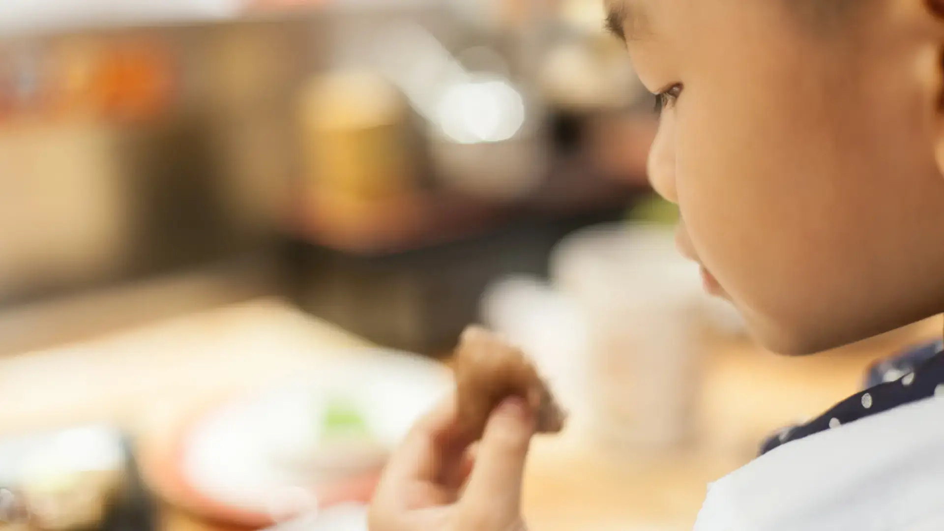 Focus on a child's face with food in his hand, hesitant to eat it