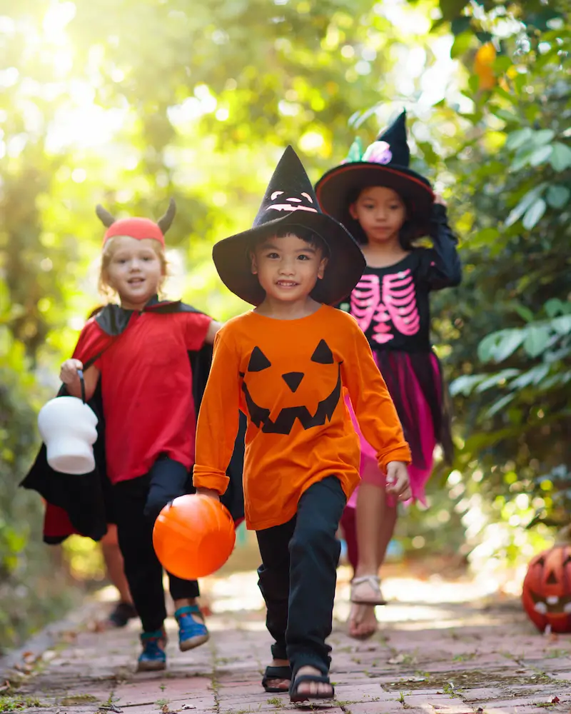 A group of three children wearing Halloween costumes and looking happy