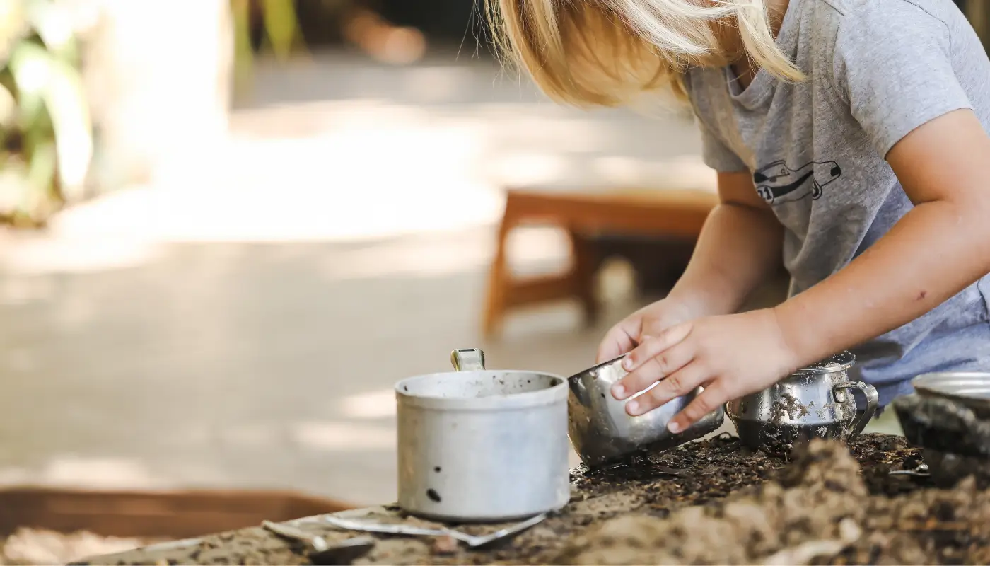 A little child playing with a mud kitchen in a garden