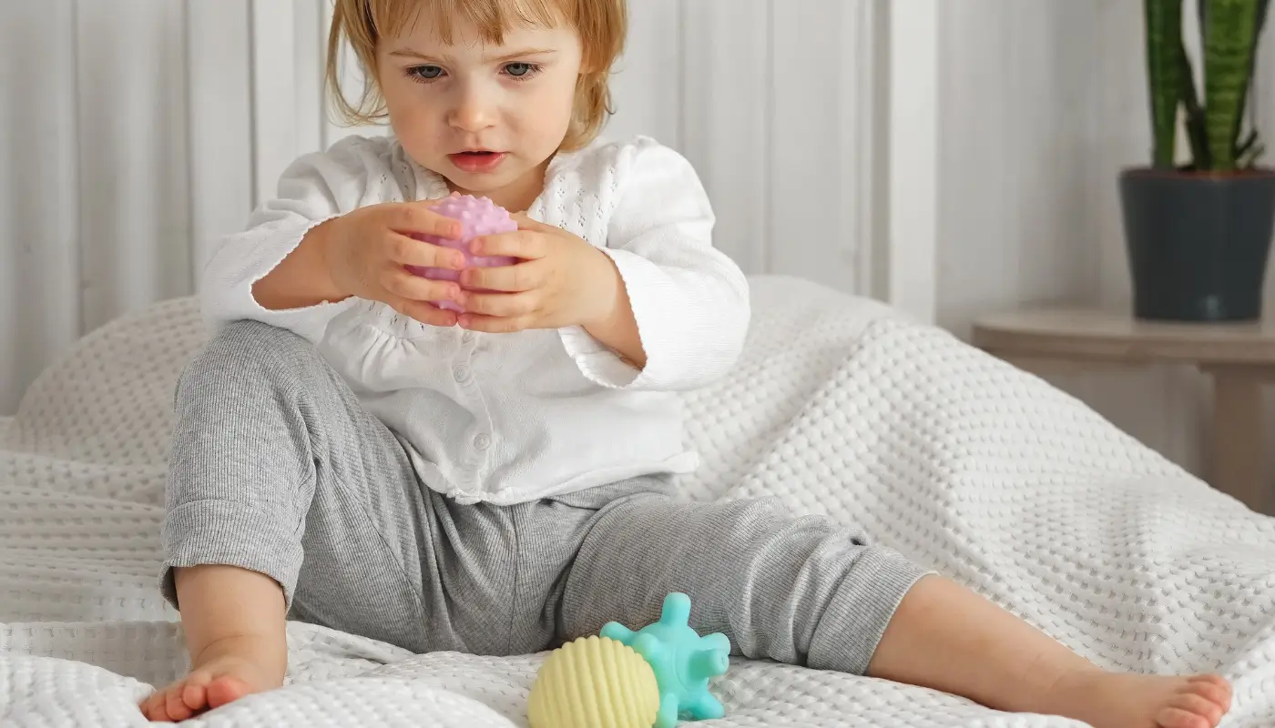 A little girl on a bed, playing with different sensory ball toys