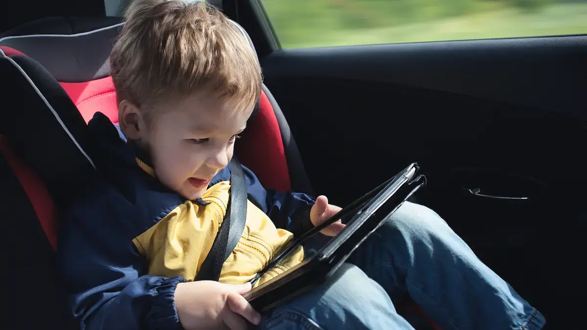 A child seating in a car, in his safety seat, playing with a table and looking entertained