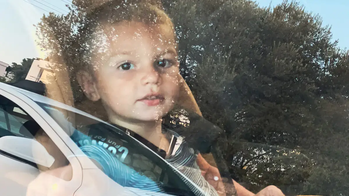 A little boy sitting in a car seat, looking through the window at the photographer