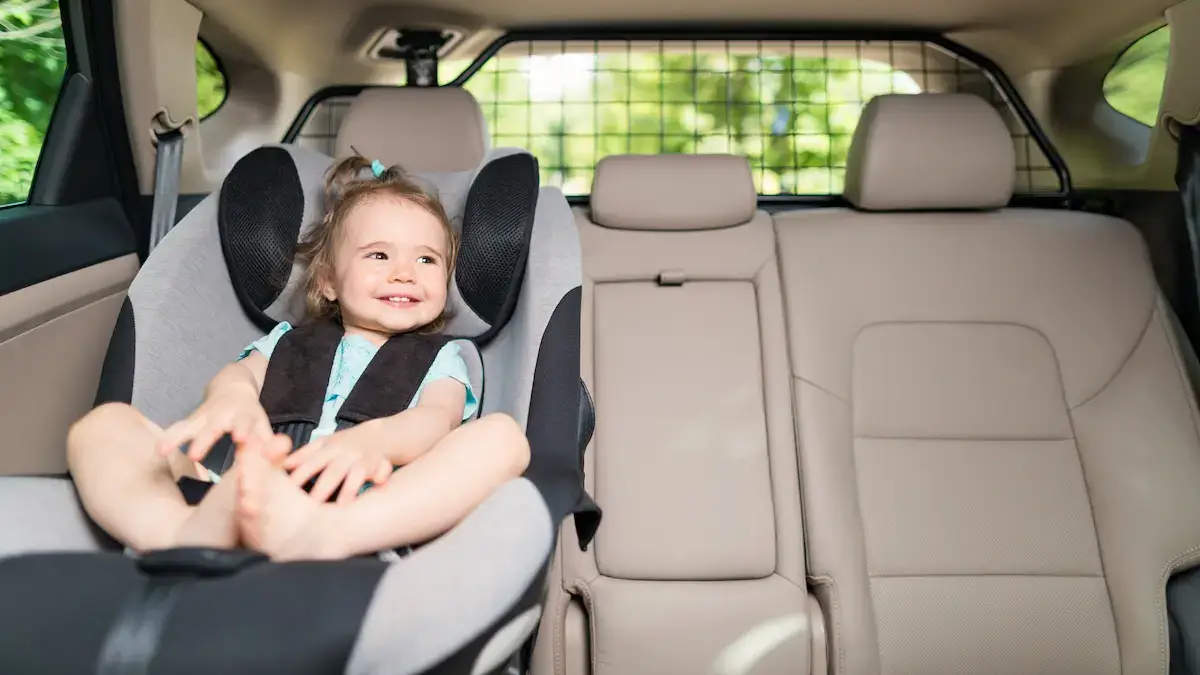 A little girl in her booster seat in a car, looking happy and smiling